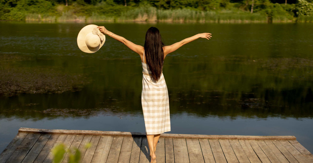 Woman on a lake dock holding a sun hat, arms open - Lake Country Outfitters, Lake Oconee